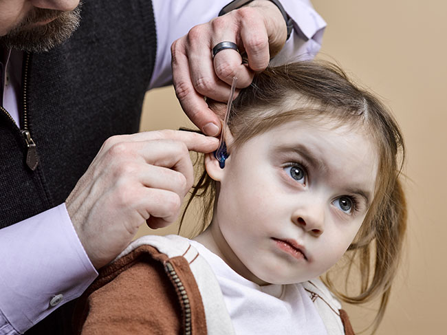 A healthcare professional is placing a hearing aid into the ear of a young girl at a pediatric appointment.