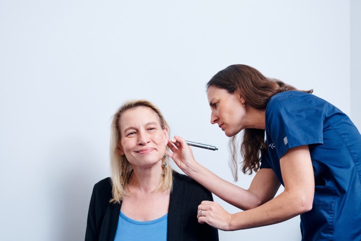 An audiologist conducts a hearing test on a female patient by placing a device near her ear.