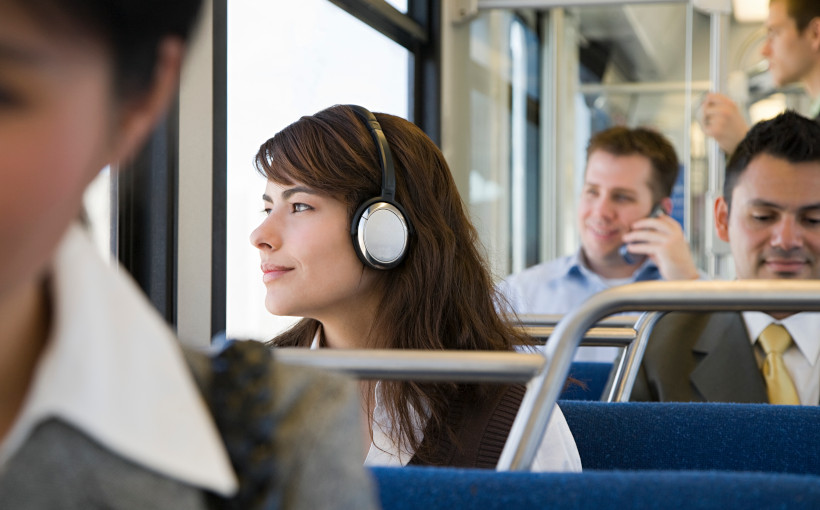A woman wears headphones while looking out the window of the city bus