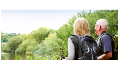 An older couple hiking through the woods with backpacks on