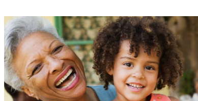 An elderly grandmother smiles while holding her smiling granddaughter